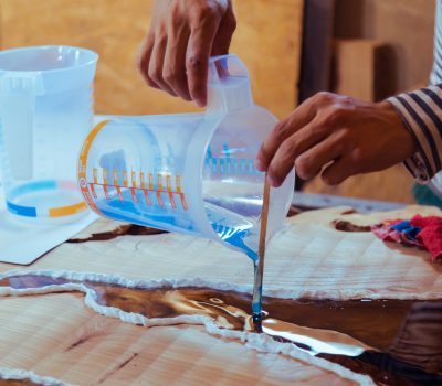 Closeup of carpenter pouring epoxy liquid in a wooden table. Process of making a craft resin and wood table